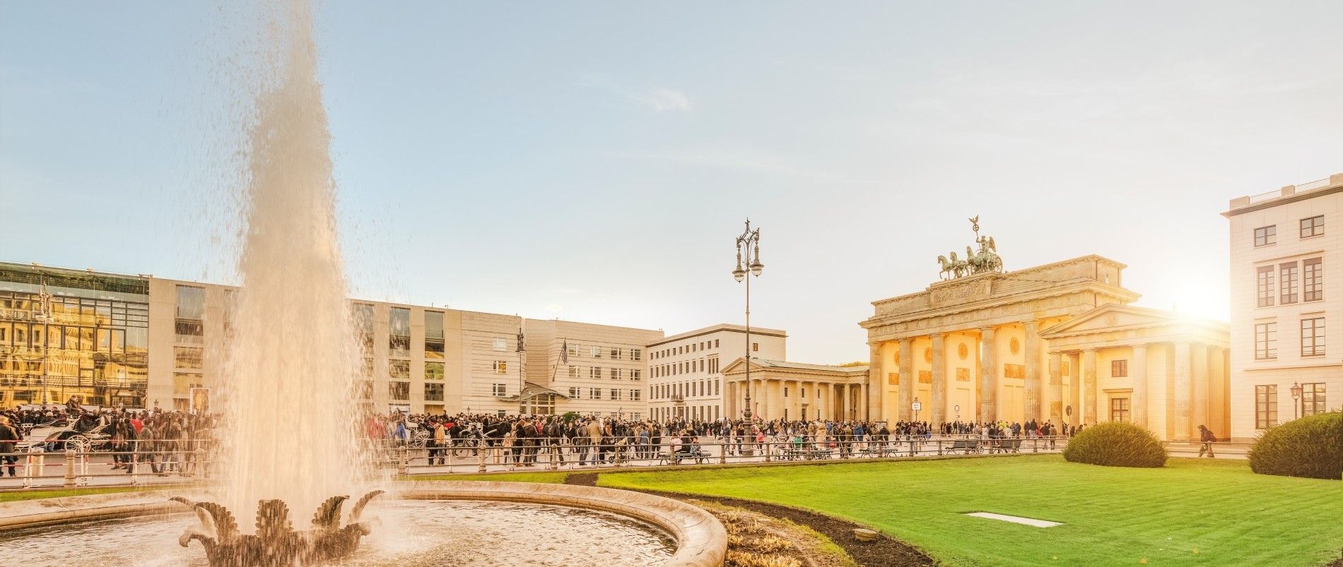 Brandenburger Tor mit Springbrunnen im Vordergrund bei Sonnenuntergang.