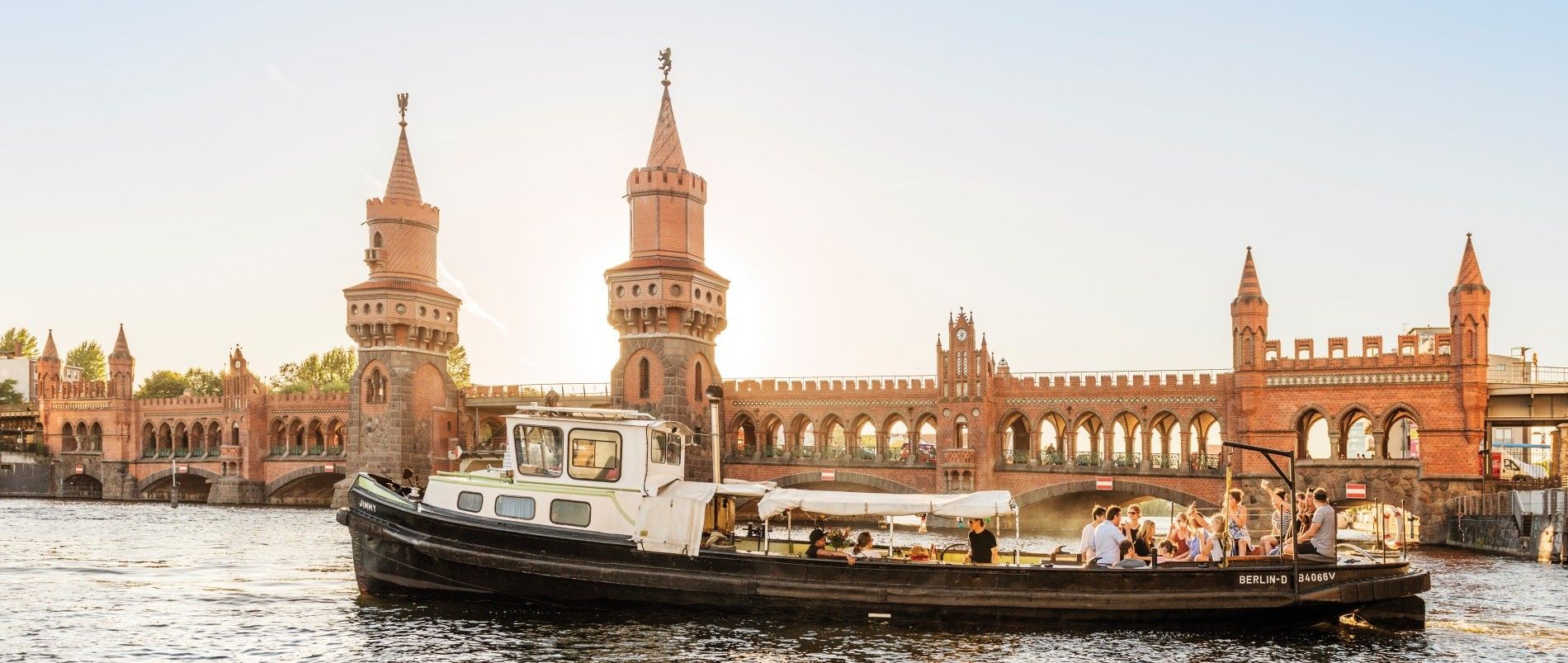 Ein Ausflugsboot fährt auf einem Fluss vor der Oberbaumbrücke in Berlin bei Sonnenuntergang.
