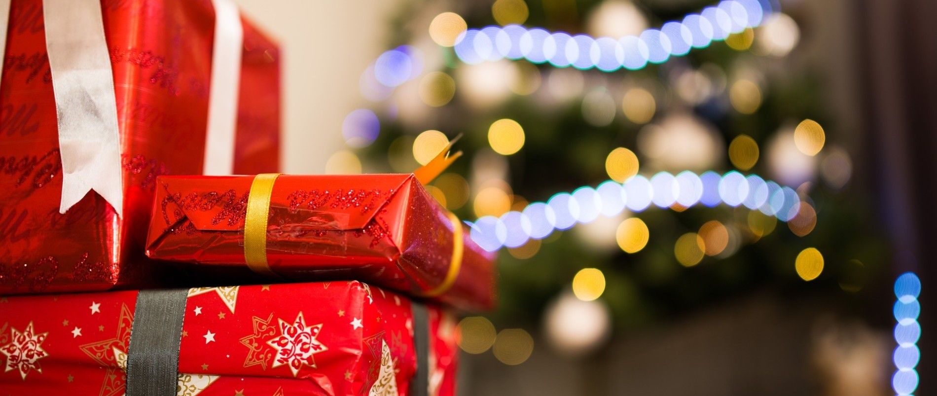 Gestapelte rote Geschenke vor einem Weihnachtsbaum mit Lichterdekoration