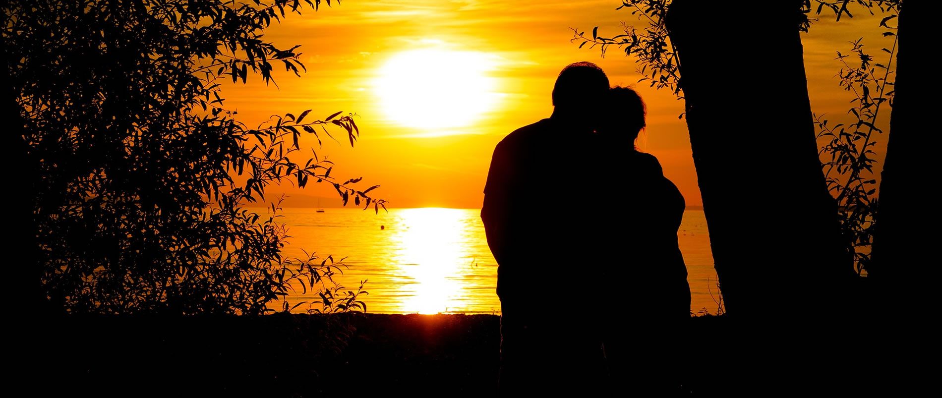 Silhouette eines Paares, das bei Sonnenuntergang am See steht.