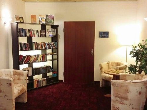 Gemütlicher Lese- und Sitzbereich mit Bücherregal, zwei Sesseln, Tisch und Zimmerpflanze.