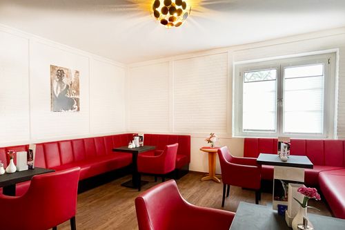 Ein einladendes Café mit roten Polstersitzen und schlichten Tischen, dekoriert mit Blumen und Wandkunst.