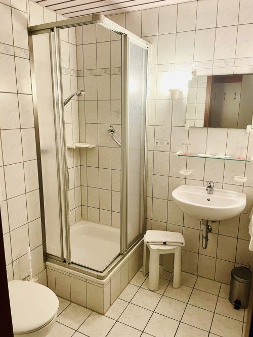 Kleines Badezimmer mit Dusche, Waschbecken und WC, gefliest in Weiß.